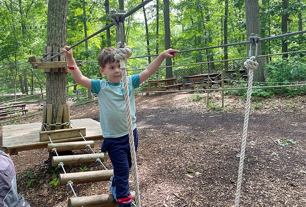 Little boy crosses rope bridge at The Adventure Playground
