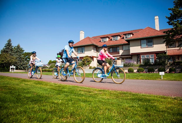 family in helmets biking in front of the Ocean's Edge Resort