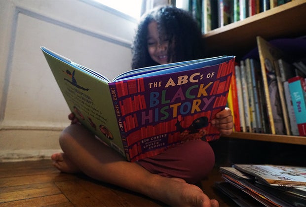 Girl smiling reading reading a black history book for children The ABCs of Black History