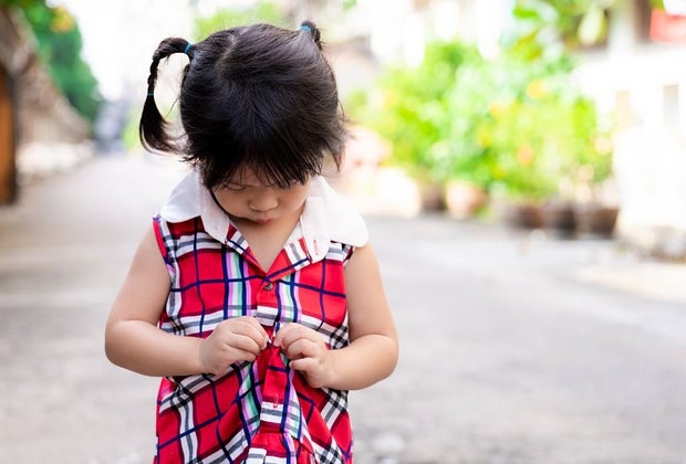 little girl plays with buttons on her dress