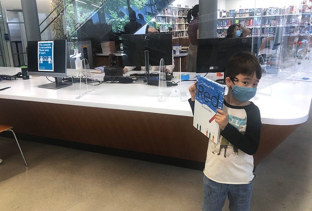 Boy holding up a book at the checkout at the greenpoint library