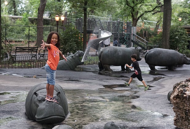 Girl standing on a play hippo at a park surrounded by trees