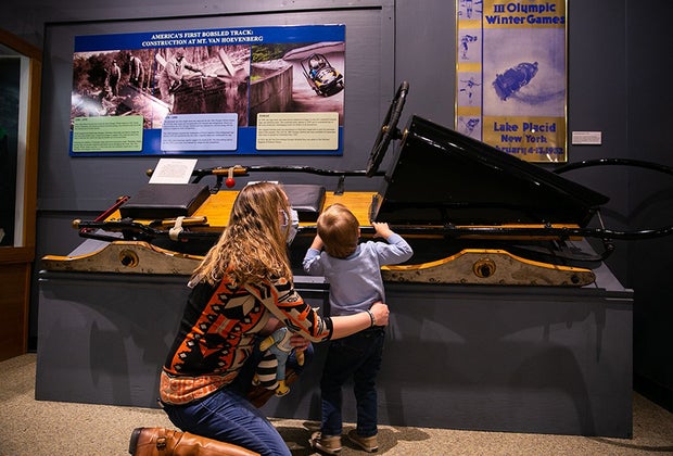 Things to do in Lake Placid with Kids: The Olympic Museum Mom and son looking at exhibit Things to Do in Lake Placid on a Winter Vacation Status message