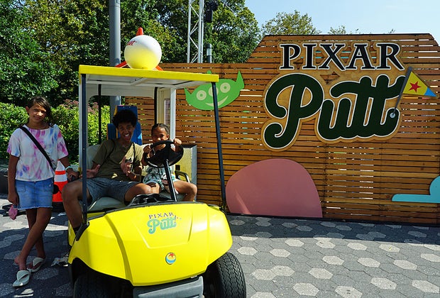 Three kids post with Pixar Putt golf cart and logo