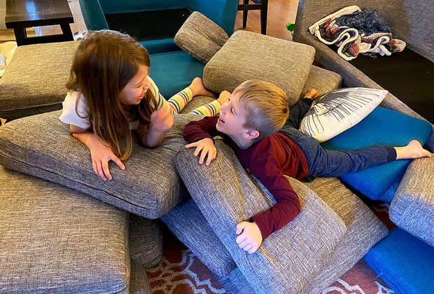 Kids giggle atop a pile of couch cushions