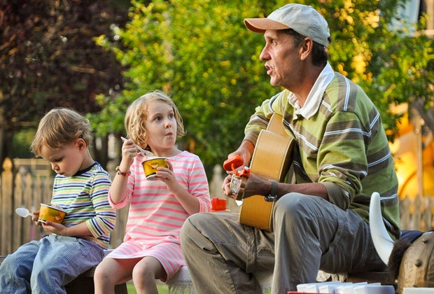 This photo shows a man playing guitar for 2 children.