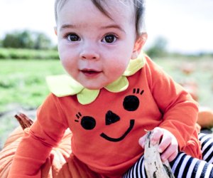 Photo of toddler wearing pumpkin costume in a pumpkin patch