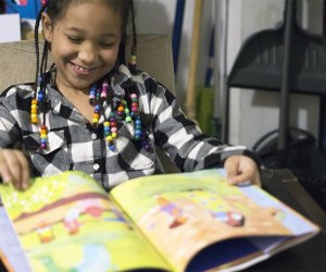 Girl smiling reading reading a black history book for children