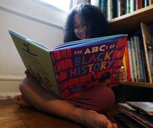 Girl smiling reading reading a black history book for children The ABCs of Black History