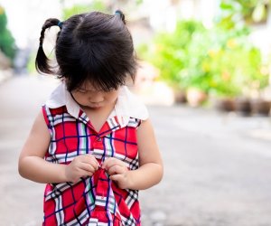 little girl plays with buttons on her dress
