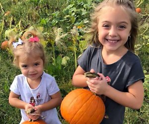 Two girls hold fresly picked pumpkins