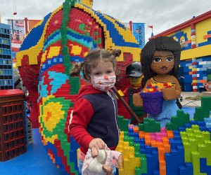 Little girl in mask poses with one of the Lego Friends