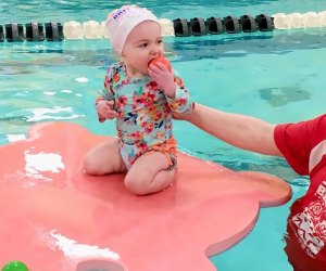 baby on lily pad in swimming pool with swimming teacher