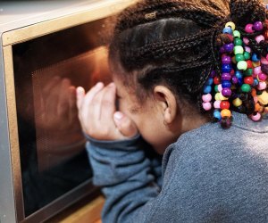 Girl peeks into microwave to check on a mug cake.