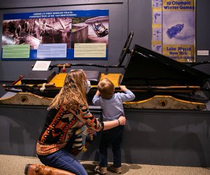  The Olympic Museum Mom and son looking at exhibit Things to Do in Lake Placid on a Winter Vacation Status message