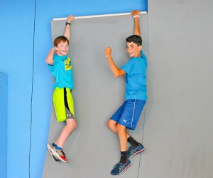 Photo of two children hanging from an obstacle course wall.