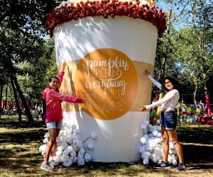 Two girls pose beside a larger-than-life pumpkin spice cup crafted out of flowers at The Fall Escape