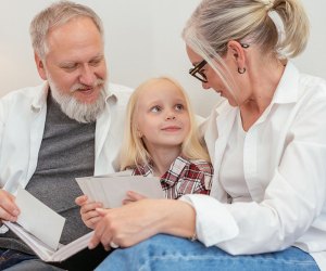 child sitting with grandparents looking through photos 101 Questions To Ask Grandparents About Their Lives