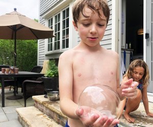 Little boy holds a bubble in his hand outside