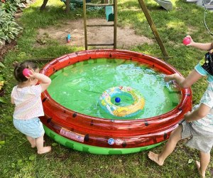 Kids throwing a ball into a little blow up pool to play water games in the backyard