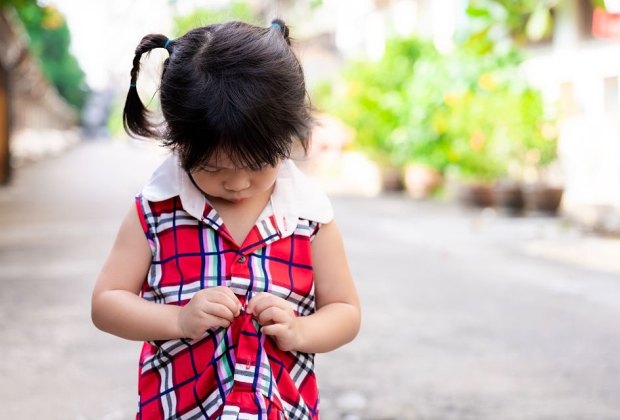 little girl plays with buttons on her dress