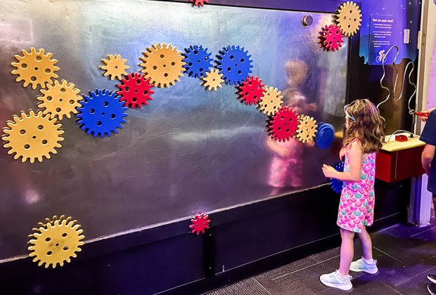 girl playing on interlocking gear wall