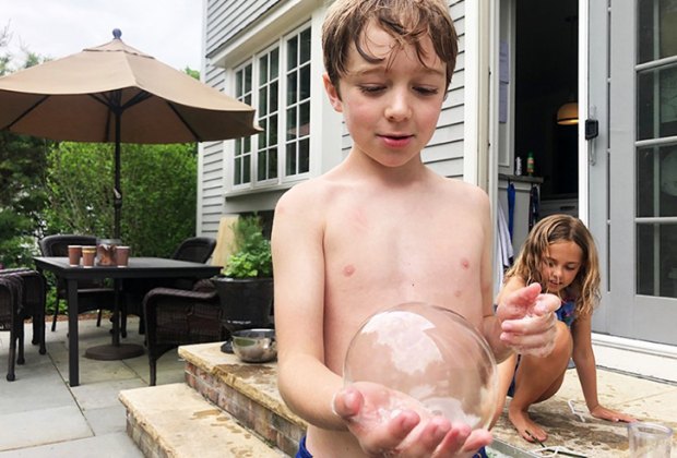 Little boy holds a bubble in his hand outside