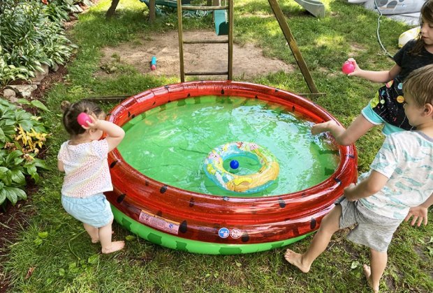 Kids throwing a ball into a little blow up pool to play water games in the backyard