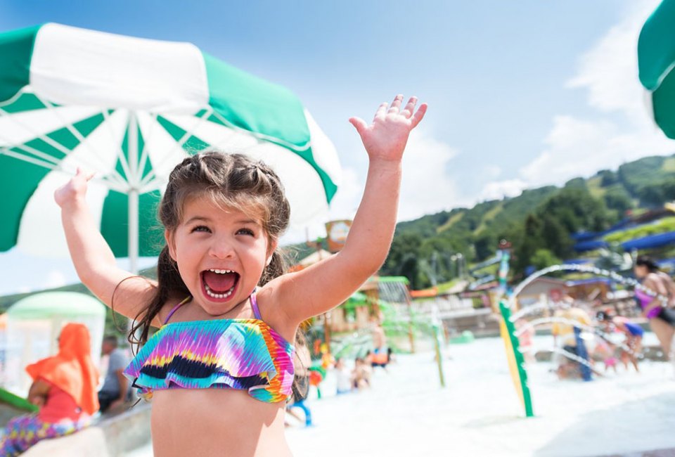 excited little girl throws up her arms in water park