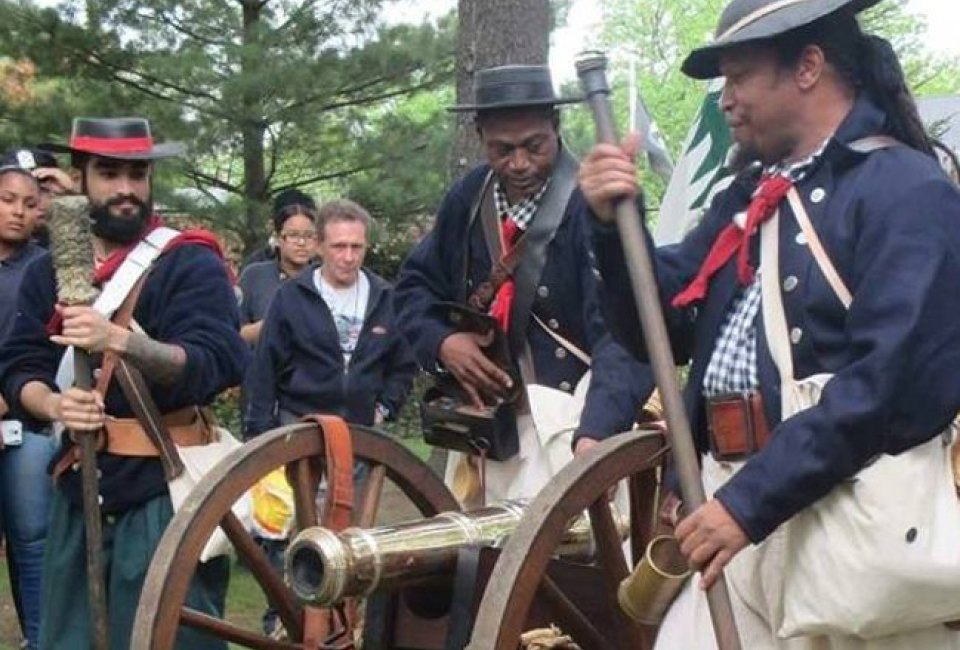 African American Revolutionary War Reenactors firing off a cannon during an encampment.